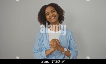 Schöne junge afroamerikanische Frau mit lockigen Haaren und gefesselten Händen, lächelt über einer isolierten weißen Hintergrundwand. Stockfoto