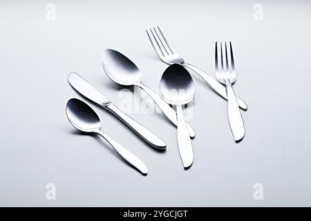 Silberfarbenes Besteck wie Löffel, Gabeln, Messer, Tassen und Teller, fotografiert auf weißem Hintergrund Stockfoto