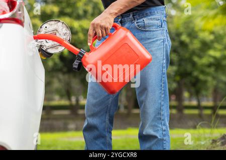 Junger Mann hält eine rote Gallone Benzin, das Reservebenzin für den Notgebrauch ist, wenn während der Fahrt der Kraftstoff ausgeht oder Reservebenzin in r verwendet wird Stockfoto