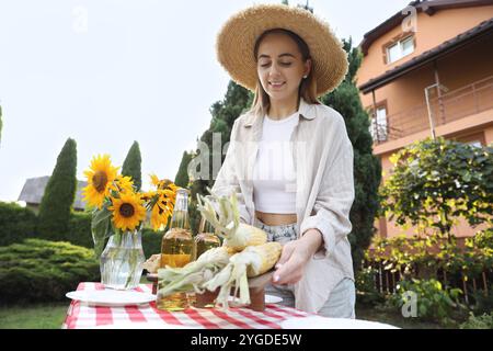 Schöne Frau mit frischen Maiskolben in der Nähe des Tisches im Garten Stockfoto