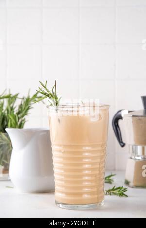 Glas aromatischer Rosmarin-Kaffee-Latte mit Eisduft, Schlagsahne oder Sahne, kaltes Kaffeegetränk mit Rosmarin-Zweig dekoriert Stockfoto