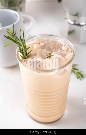 Glas aromatischer Rosmarin-Kaffee-Latte mit Eisduft, Schlagsahne oder Sahne, kaltes Kaffeegetränk mit Rosmarin-Zweig dekoriert Stockfoto