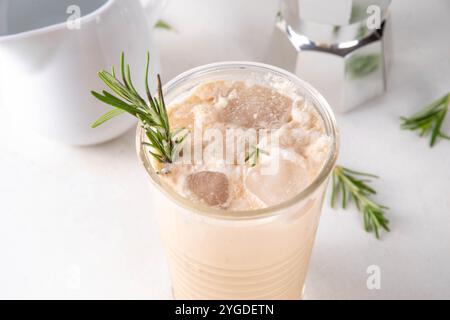 Glas aromatischer Rosmarin-Kaffee-Latte mit Eisduft, Schlagsahne oder Sahne, kaltes Kaffeegetränk mit Rosmarin-Zweig dekoriert Stockfoto