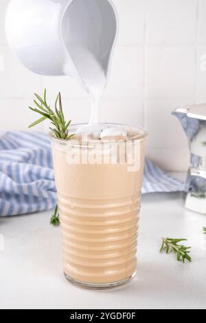 Glas aromatischer Rosmarin-Kaffee-Latte mit Eisduft, Schlagsahne oder Sahne, kaltes Kaffeegetränk mit Rosmarin-Zweig dekoriert Stockfoto