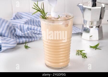 Glas aromatischer Rosmarin-Kaffee-Latte mit Eisduft, Schlagsahne oder Sahne, kaltes Kaffeegetränk mit Rosmarin-Zweig dekoriert Stockfoto