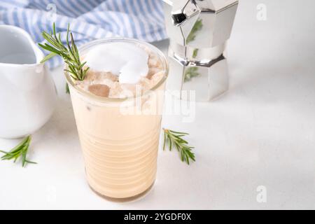 Glas aromatischer Rosmarin-Kaffee-Latte mit Eisduft, Schlagsahne oder Sahne, kaltes Kaffeegetränk mit Rosmarin-Zweig dekoriert Stockfoto