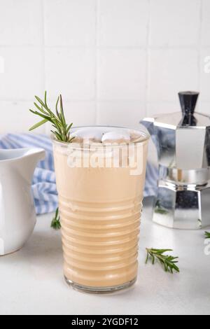 Glas aromatischer Rosmarin-Kaffee-Latte mit Eisduft, Schlagsahne oder Sahne, kaltes Kaffeegetränk mit Rosmarin-Zweig dekoriert Stockfoto