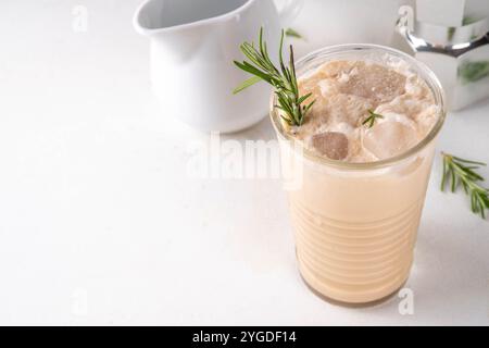 Glas aromatischer Rosmarin-Kaffee-Latte mit Eisduft, Schlagsahne oder Sahne, kaltes Kaffeegetränk mit Rosmarin-Zweig dekoriert Stockfoto