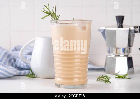 Glas aromatischer Rosmarin-Kaffee-Latte mit Eisduft, Schlagsahne oder Sahne, kaltes Kaffeegetränk mit Rosmarin-Zweig dekoriert Stockfoto