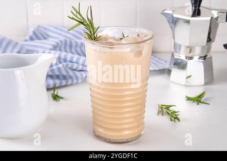 Glas aromatischer Rosmarin-Kaffee-Latte mit Eisduft, Schlagsahne oder Sahne, kaltes Kaffeegetränk mit Rosmarin-Zweig dekoriert Stockfoto