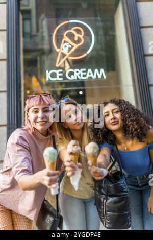 Vertikales Porträt von drei verschiedenen modernen Frauen, die mit Eiskegeln auf der Straße toasten Stockfoto