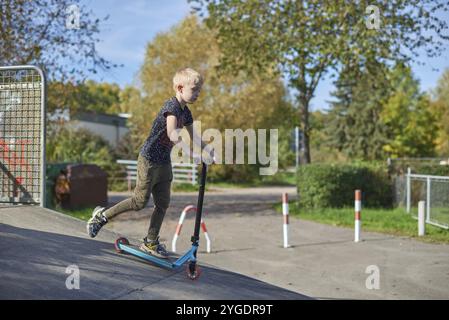 Boy on Scooter macht einen Trick und genießt seine Fahrt im Skatepark am bewölkten Frühlingstag. Junger Mann macht Trick auf dem Tretroller im Park. Fu Stockfoto