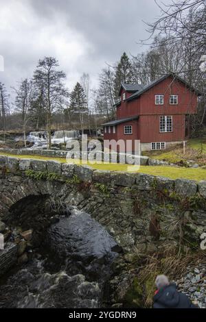 Wunderschönes rotes schwedisches Haus. Ehemalige Wassermühle an einem Fluss mit einem kleinen Wasserfall. Sonnenuntergang in einer wunderschönen Landschaft mit einem Holzhaus in Schweden, Skandi Stockfoto