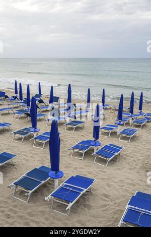 Leere Strandliegen und geschlossene Sonnenschirme am menschenleeren Strand in der Nebensaison Stockfoto