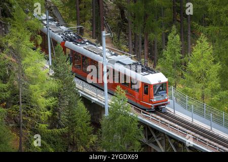 Zermatt, Schweiz, 7. Oktober 2019: Roter Gornergrat-Touristenzug auf der Brücke, Dorfhäuser und Schweizer Alpenpanorama, Europa Stockfoto