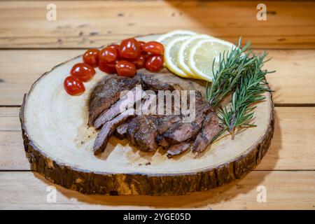 Steak Slice auf dem Holzteller, Decoration by Lemon Slice, Tomate und Rosmarin auf dem Holztisch in dezentes Licht-Ambiente. Stockfoto