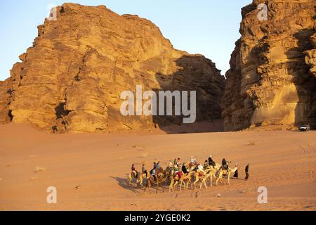 Jordanien, Wadi Rum, 2. November 2022: Kamelkarawane mit Touristen in der Wüste, Felsenberge bei Sonnenuntergang, Asien Stockfoto