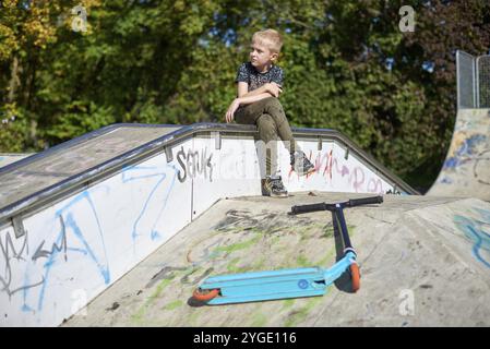 Kind auf Kick scooter im Park. Kinder lernen roller Board zu skaten. Kleiner Junge Schlittschuhlaufen auf sonnigen Sommertag. Aktivität im Freien für Kinder zum sicheren Residenzappartementhaus Stockfoto