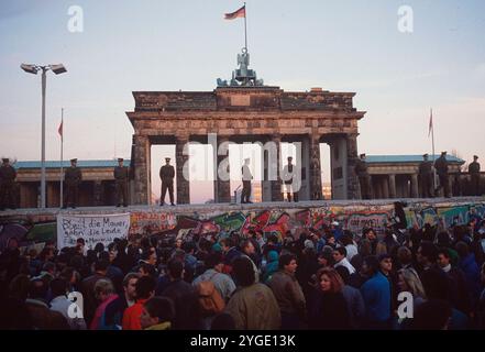 ARCHIVFOTO: Vor 35 Jahren, am 9. November 1989, fiel die Berliner Mauer. Das Brandenburger Tor mit der „Mauer“ im Vordergrund. Die Polizisten der Menschen stehen auf der Mauer, und unter ihnen stehen viele Menschen vor der Mauer; Landschaftsformat. ? Stockfoto