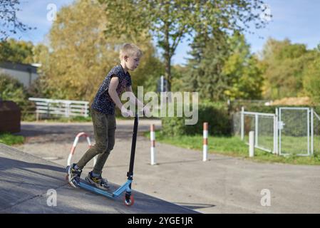 Kind auf Kick scooter im Park. Kinder lernen roller Board zu skaten. Kleiner Junge Schlittschuhlaufen auf sonnigen Sommertag. Aktivität im Freien für Kinder zum sicheren Residenzappartementhaus Stockfoto