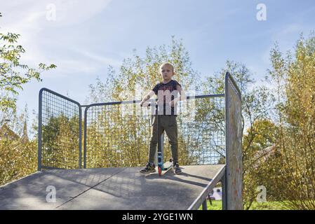 Boy on Scooter macht einen Trick und genießt seine Fahrt im Skatepark am bewölkten Frühlingstag. Junger Mann macht Trick auf dem Tretroller im Park. Fu Stockfoto