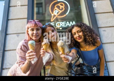 Drei Schönheitsfrauen, die vor dem Laden köstliche Eissorten halten Stockfoto