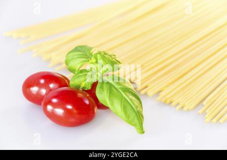 Ungekochte Pasta-Spaghetti, rote leckere Tomaten und grüne Basilikumblätter auf weißem Tisch Stockfoto