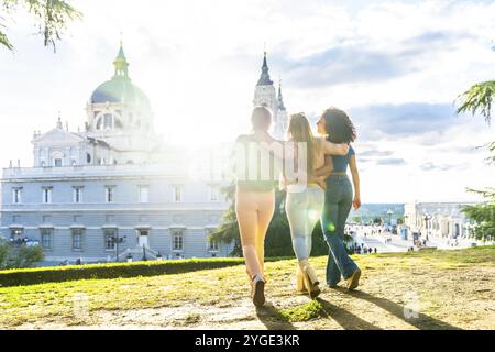 Rückansicht von drei Freundinnen, die gegen Sonnenuntergang auf einem Aussichtspunkt der Stadt spazieren Stockfoto