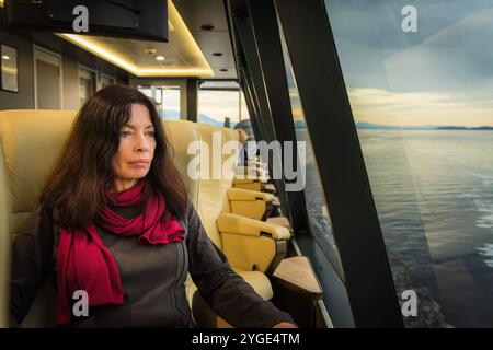 Eine einzige weibliche Touristenin sitzt auf einem weichen Sessel, der nach außen geneigt und nach vorne gerichtet ist, in vollkommenem Komfort und genießt eine Bootstour auf dem Gordon River. Stockfoto