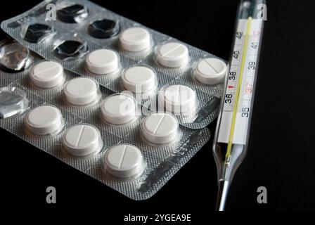 Nahaufnahme von Thermometer- und Paracetamol-Pillen, isoliert auf schwarzem Hintergrund. Stockfoto