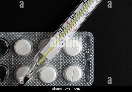 Detaillierte Darstellung von Paracetamol-Pillen mit Thermometer, die die Gesundheitsversorgung und die Erkältungs-/Grippebehandlung betonen, vor einem dunklen, kontrastierenden Hintergrund. Stockfoto