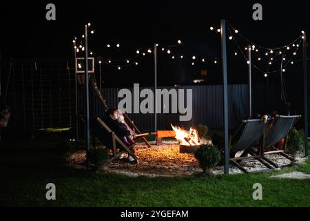 Eine ruhige Nachtszene im Freien mit bequemen Sitzgelegenheiten am Lagerfeuer, beleuchtet von sanften Lichtern. Die Einrichtung schafft eine friedliche und Co Stockfoto