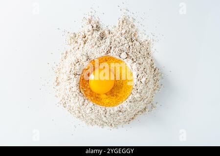 Ein rohes Ei mit Eigelb auf einem Hügel Vollkornmehl. Backkonzept Stockfoto