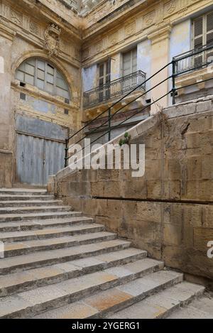 Valletta. Eisentür. Heruntergekommen. Wellblech. Haus. Erker. Kalkstein. bay-Fenster. Treppen. Treppe. Renovierungsbedürftig. Alt. Marode. alt. Kunstbügeltür. Stockfoto