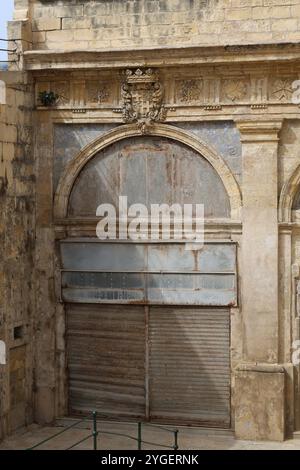 Valletta. Eisentür. Heruntergekommen. Wellblech. Haus. Erker. Kalkstein. bay-Fenster. Treppen. Treppe. Renovierungsbedürftig. Alt. Marode. alt. Kunstbügeltür. Stockfoto