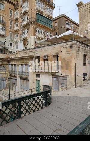 Valletta. Eisentür. Heruntergekommen. Wellblech. Haus. Erker. Kalkstein. bay-Fenster. Treppen. Treppe. Renovierungsbedürftig. Alt. Marode. alt. Kunstbügeltür. Stockfoto