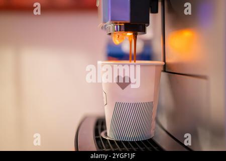 Kaffeemaschine macht Kaffee in einer Papptasse auf einer öffentlichen Veranstaltung, Bankett, ohne Personen. Kaffeemaschine, die eine Tasse mit Espresso füllt. Stockfoto