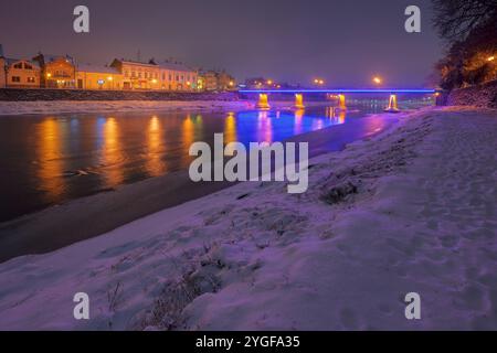 uschhorod, ukraine - 26. Dezember 2016: Nachtszene des uzh-Flusses. Das Licht der Innenstadt spiegelt sich im Wasser. Schnee am Ufer Stockfoto