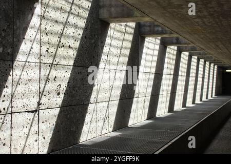 Betonwand mit abgewinkelten Licht- und Schattenmustern, die einen beeindruckenden geometrischen Effekt in einem minimalistischen, modernen architektonischen Ambiente schaffen. Stockfoto