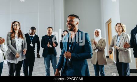 Ein freudiger Geschäftsmann, der einen erfolgreichen Workshop leitet und mit seinem Team spricht und interagiert. Er ist von glücklichen Kollegen umgeben und schafft eine Zusammenarbeit Stockfoto