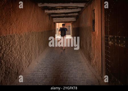 Ein männlicher Tourist, der eine enge Straße in der alten Medina hinunterläuft, rustikale charmante Wände in Tunnelallee, Alleinreisender, der Marrakesch, Marokko, erkundet Stockfoto