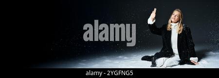 Die schöne junge Frau sitzt ruhig im Schnee und fängt die Essenz der winterlichen Eleganz ein. Stockfoto