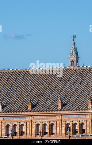 Ein lebhafter Blick auf die Skyline des Turms La Giralda, der hinter einem historischen Dach in Sevilla, Spanien, ragt. Hellblauer Himmel ergänzt die architektonische Deta Stockfoto