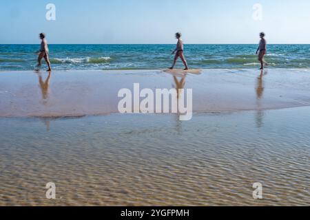 Drei Personen, die entlang der Küste am Playa de Cuesta Maneli in Huelva, Andalusien, spazieren. Die ruhige Strandlandschaft fängt Bewegungen und Reflexionen ein Stockfoto