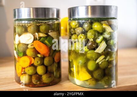 Zwei Gläser traditioneller eingelegter Oliven im andalusischen Stil, die zu Hause hergestellt werden, mit lebhaften Farben und frischen Zutaten aus Sevilla. Perfekte Repräsenta Stockfoto