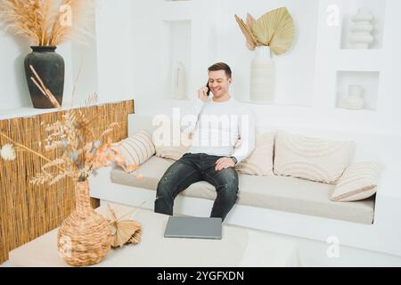 Ein junger Mann sitzt zu Hause auf dem Sofa und arbeitet ferngesteuert an einem Laptop. Stockfoto