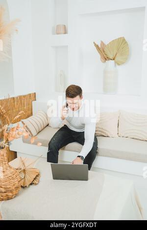 Ein junger Mann sitzt zu Hause auf dem Sofa und arbeitet ferngesteuert an einem Laptop. Stockfoto