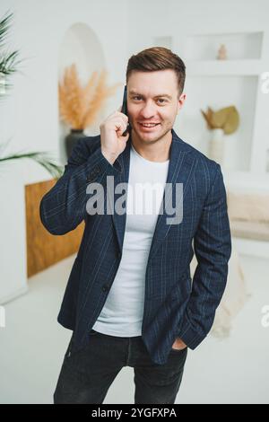 Ein junger, lächelnder Mann in einer Jacke spricht am Telefon. Emotionen des Lachens, wenn man am Telefon spricht. Ein erfolgreicher Mann arbeitet aus der Ferne am Telefon. Stockfoto