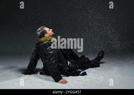 Ein junger Mann entspannt sich im Schnee und beobachtet, wie Schneeflocken sanft um ihn fallen. Stockfoto