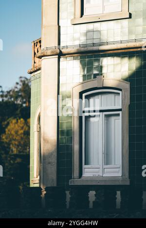 Fassade eines historischen Gebäudes mit grünen Keramikfliesen, komplizierten architektonischen Details und weiß gerahmten Bogenfenstern, die das Sonnenlicht reflektieren; ein Balkon Stockfoto